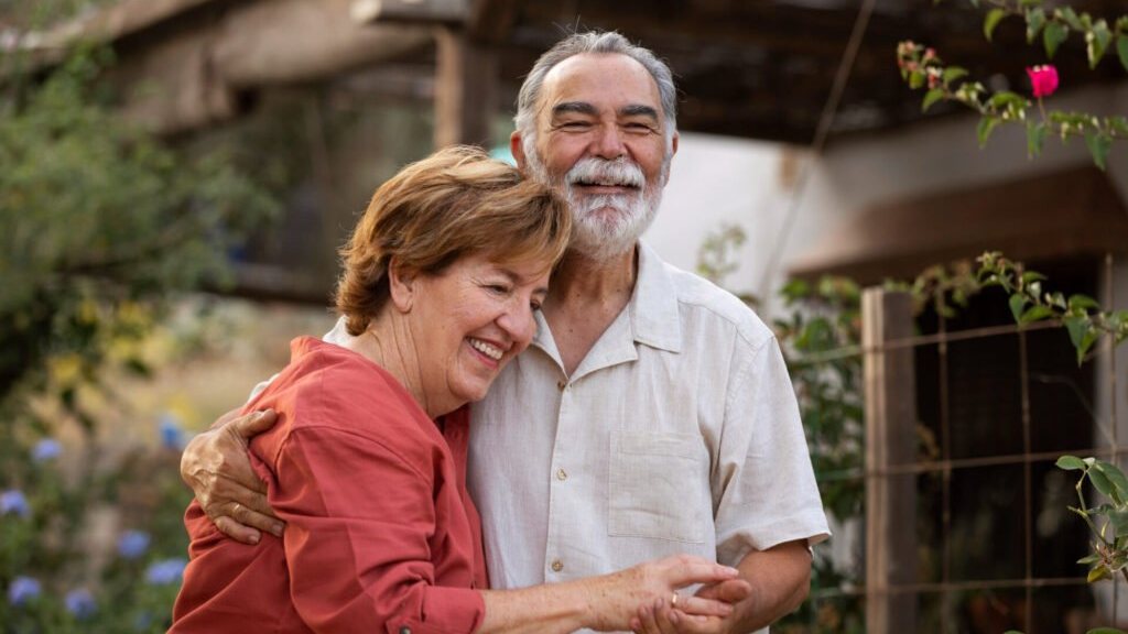 Casal de idosos sorrindo, abraçados, num jardim